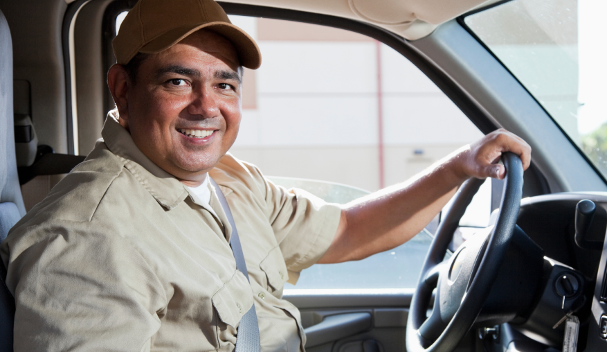 A delivery worker sitting in the driver’s side of a vehicle, smiling.